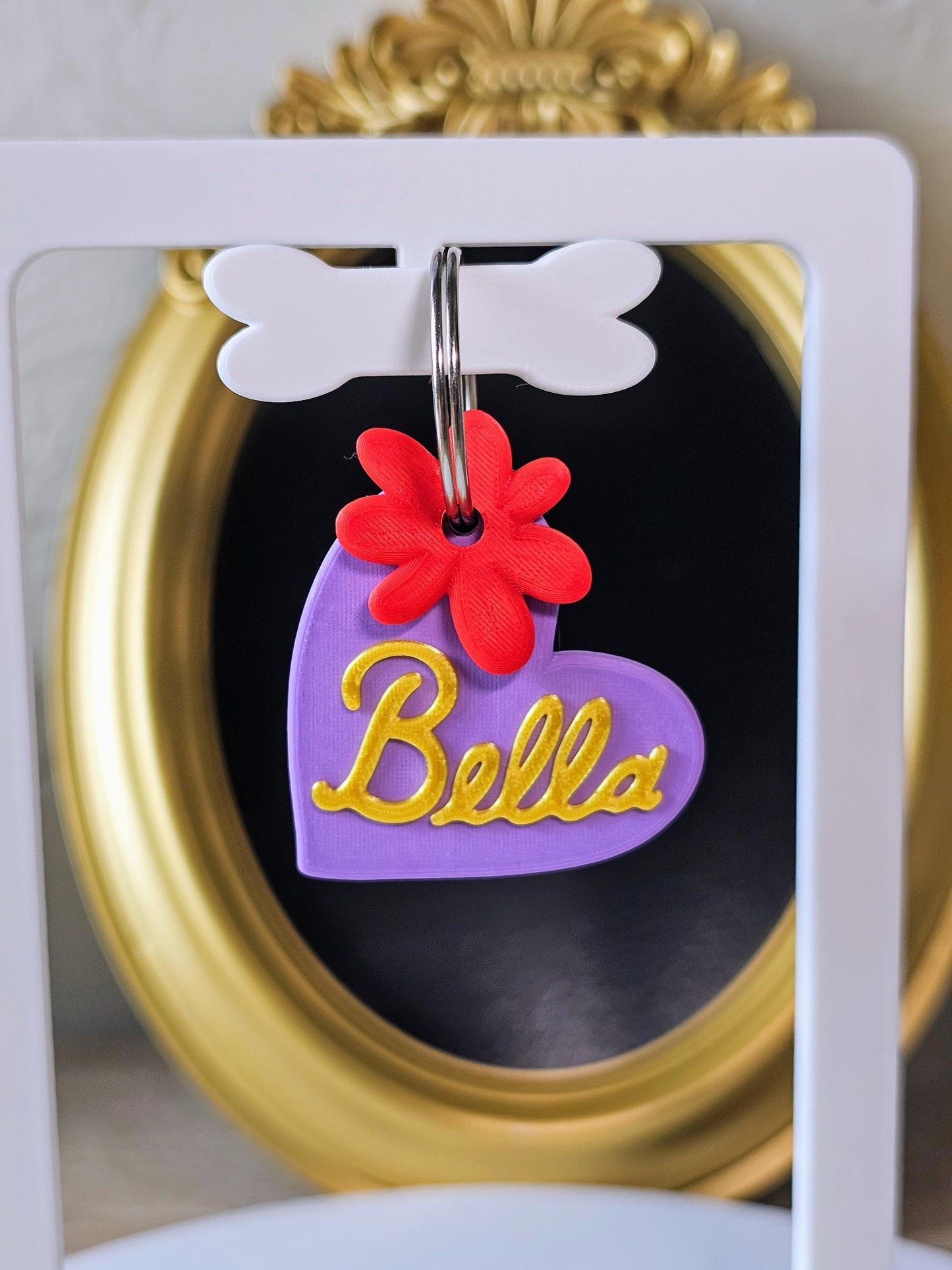Purple heart tag with the name Bella in gold and a red flower charm