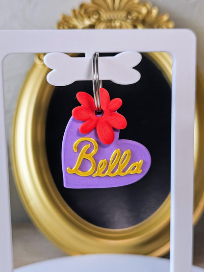 Purple heart tag with the name Bella in gold and a red flower charm