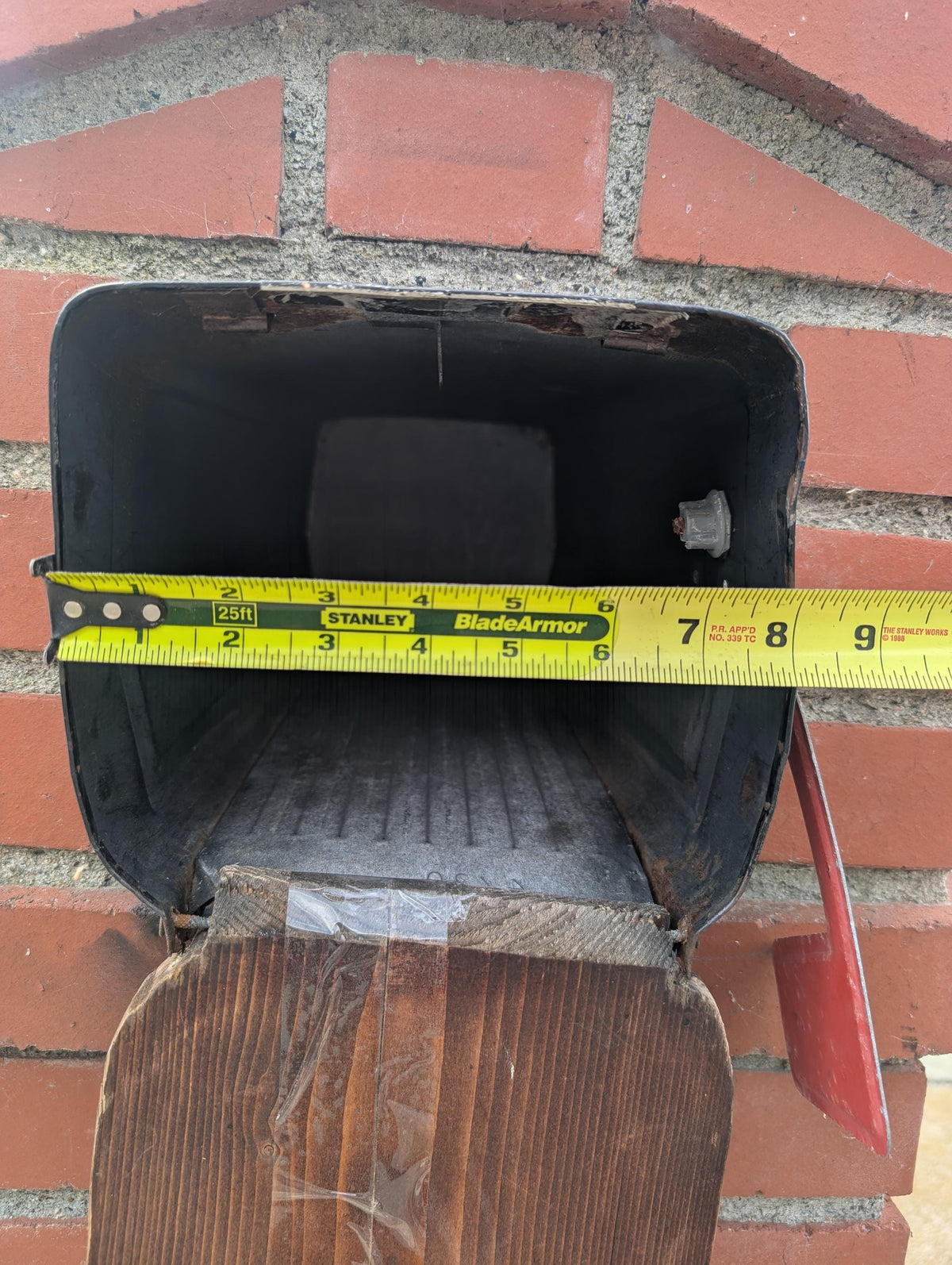 Square metal mailbox in a brick column with a tape measure across the opening