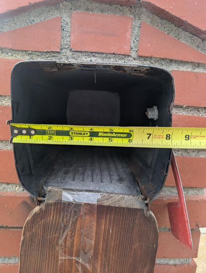 Square metal mailbox in a brick column with a tape measure across the opening